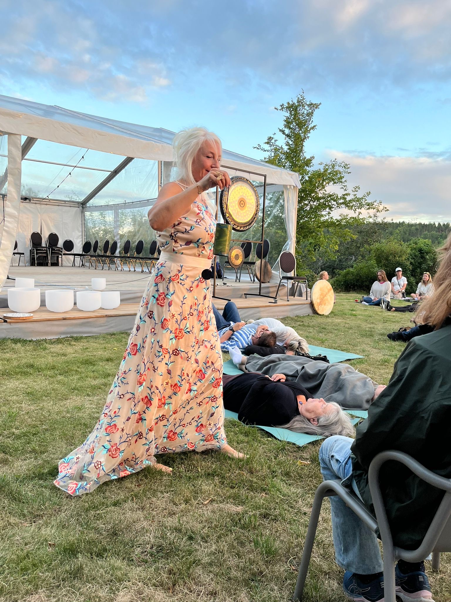 Aurelina in a long floral dress performing outdoors while festival participants rest on mats